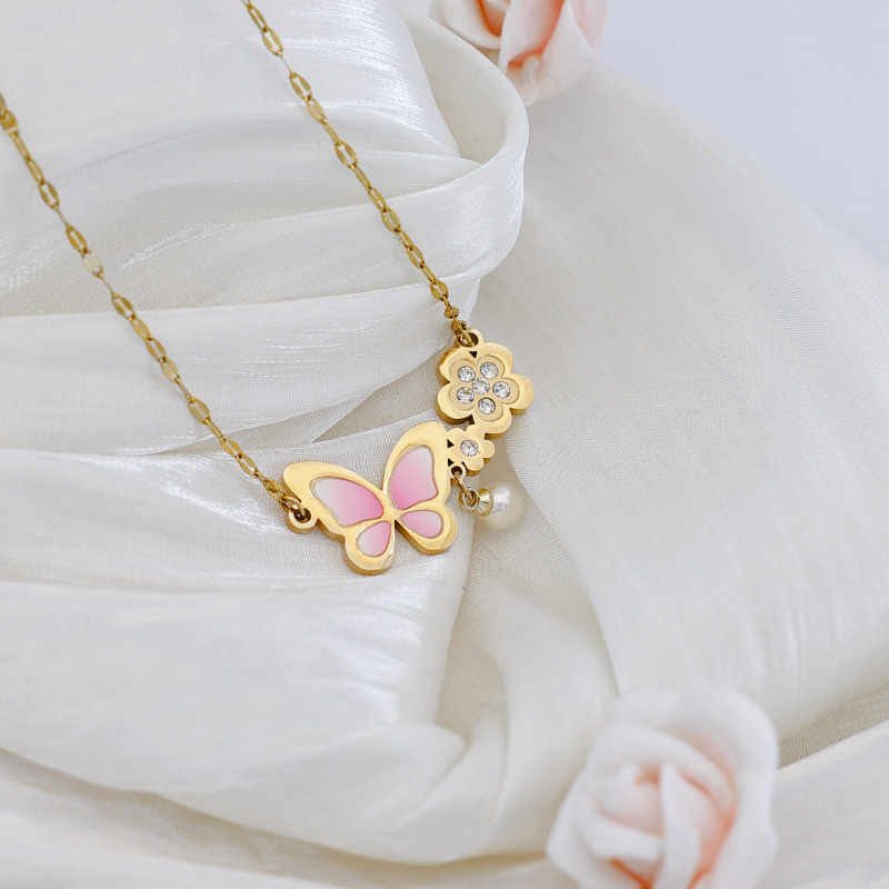 Aesthetic Pink Butterfly Jewelry - Soft Texture View Feminine pink butterfly floral necklace laid on soft white fabric, showcasing its 18k gold plated finish.