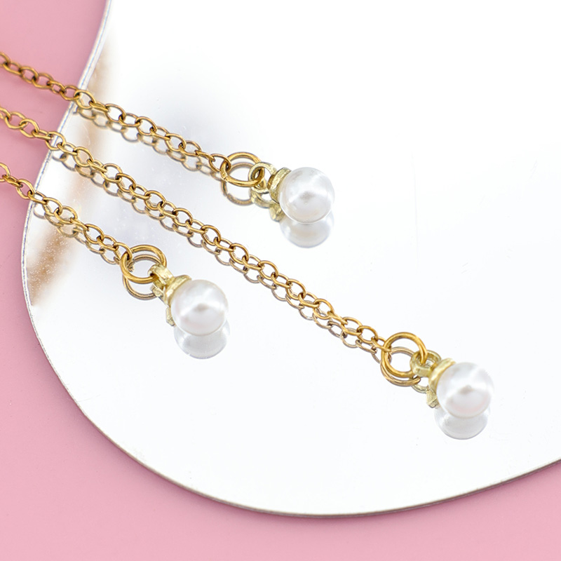 Delicate Pearl Drop Chains | High-Quality Pearl Tassel Details Macro shot of delicate gold chains with small white pearl charms at the ends, part of a moon necklace.