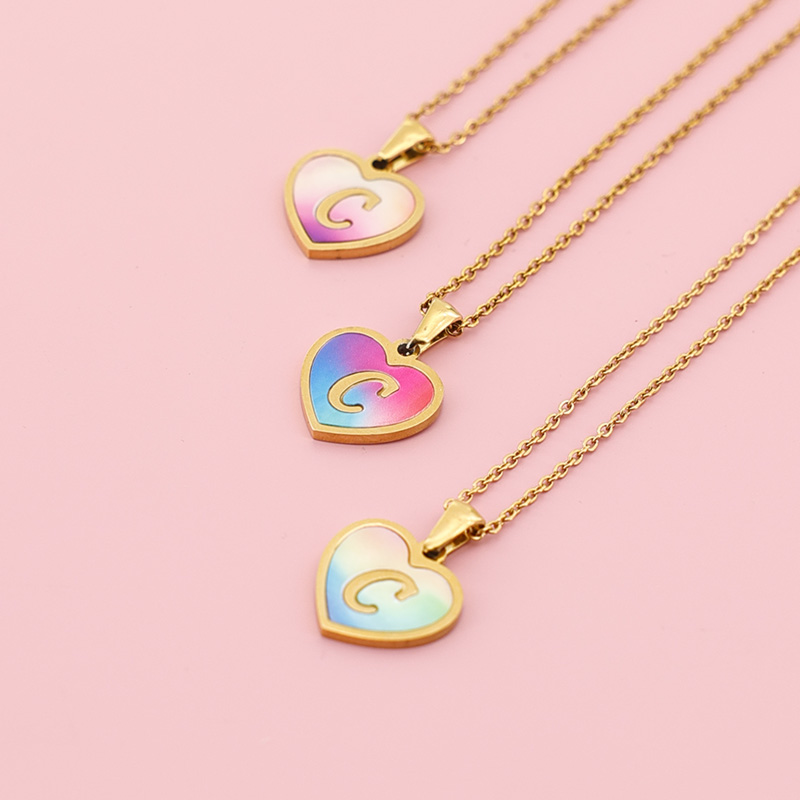 Personalized Initial Jewelry Collection | Perfect Best Friend Gift A collection of three initial heart necklaces in different gradient colors laid on a soft pink background.