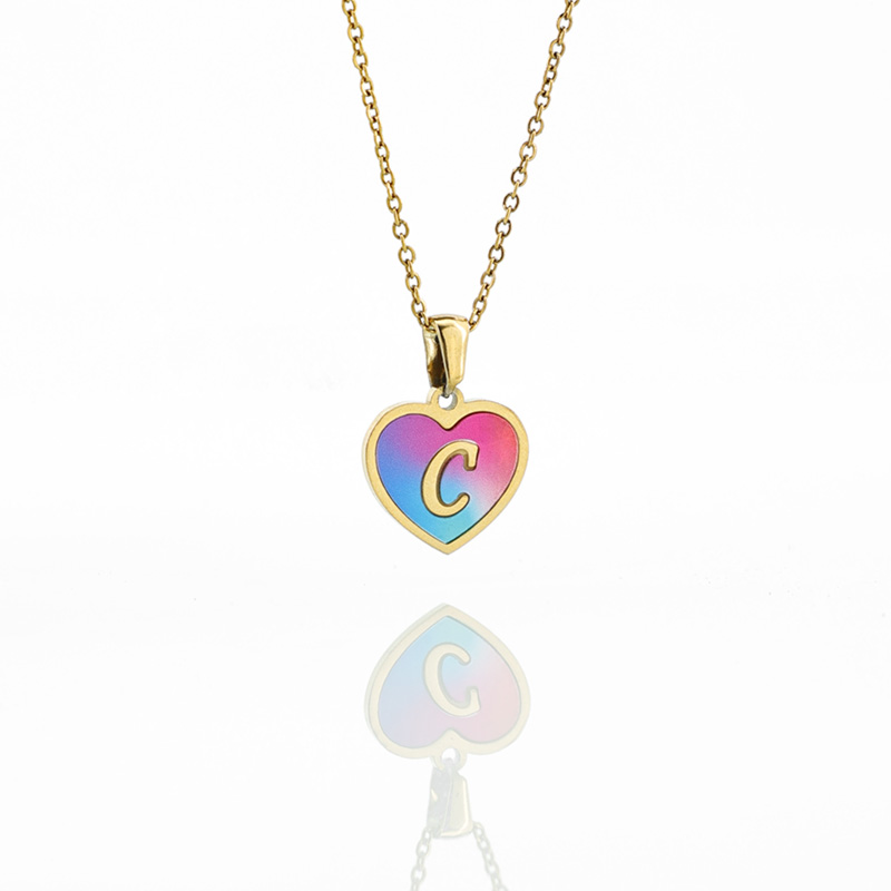Blue & Pink Gradient Initial Heart Necklace A gold heart necklace featuring a letter C initial on a vibrant blue and pink gradient enamel background, reflecting on a white surface.
